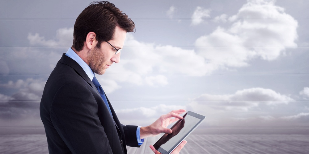 Businessman standing while using a tablet pc against clouds in a room.jpeg